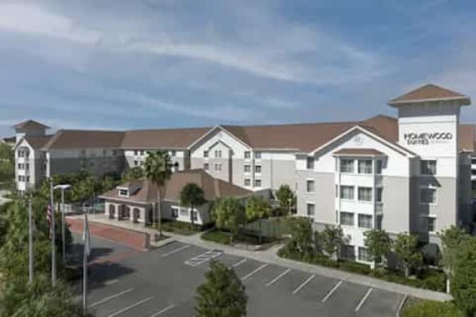 Homewood Suites by Hilton near Orlando Airport, featuring a welcoming exterior with warm afternoon lighting and a spacious parking area.