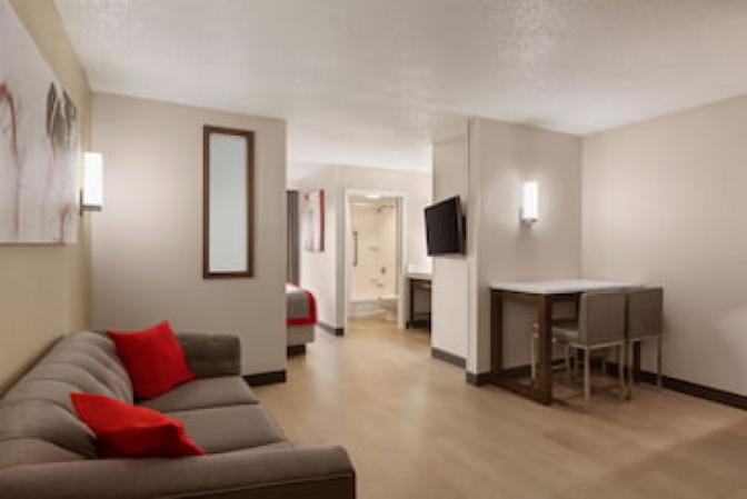 Modern king room at Ramada Suites featuring a comfortable grey couch and dining table.