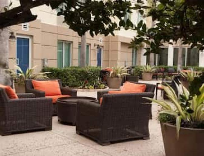 Hilton Garden Inn Orlando Airport Hotel outdoor patio with wicker chairs and orange cushions arranged around a table, surrounded by plants and greenery.