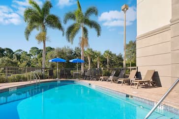 Hampton Inn hotel pool with clear blue water, surrounded by a sun deck with lounge chairs and tables under umbrellas.