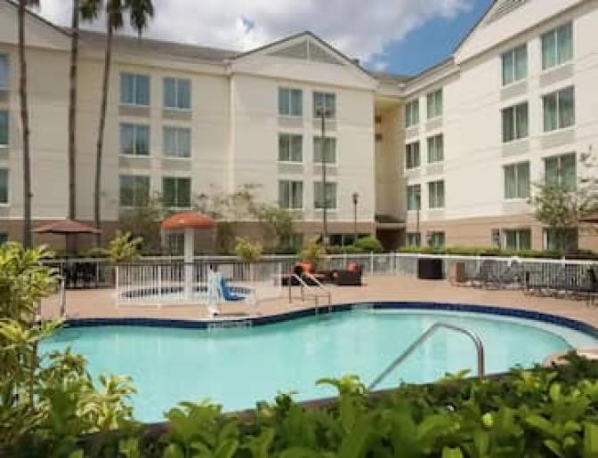 Outdoor pool area at a hotel, including a splash pad for children, lounge chairs, and potted plants.