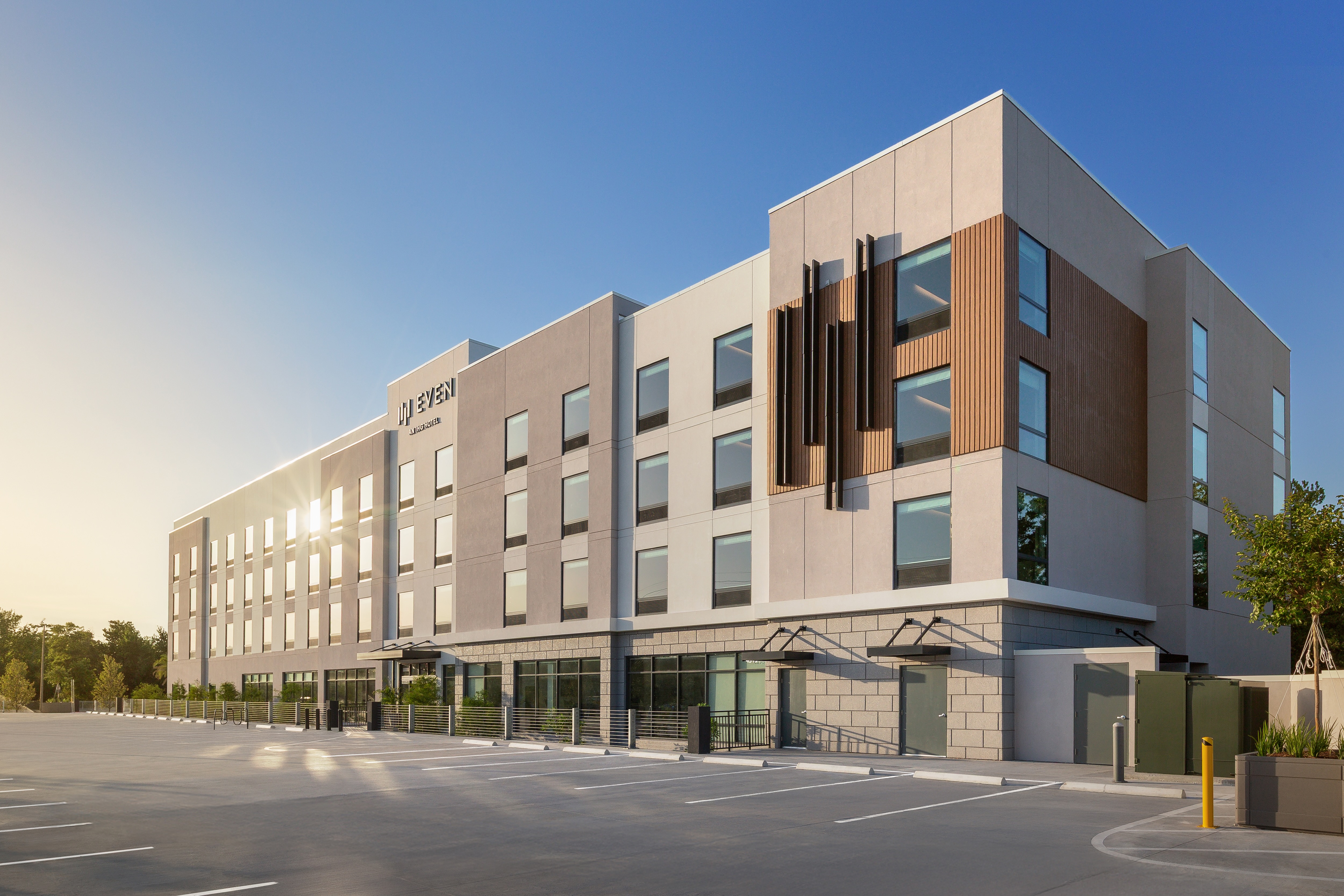 Modern exterior of EVEN Hotel during daylight, showcasing a four-story building with geometric design elements, large grid windows, and an expansive guest parking area.