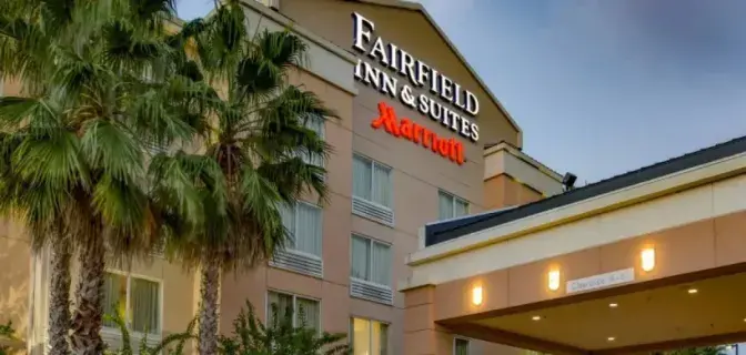 Exterior view of Fairfield Inn & Suites by Marriott Titusville, featuring a beige building with large windows, a covered entrance, and palm trees in the foreground.