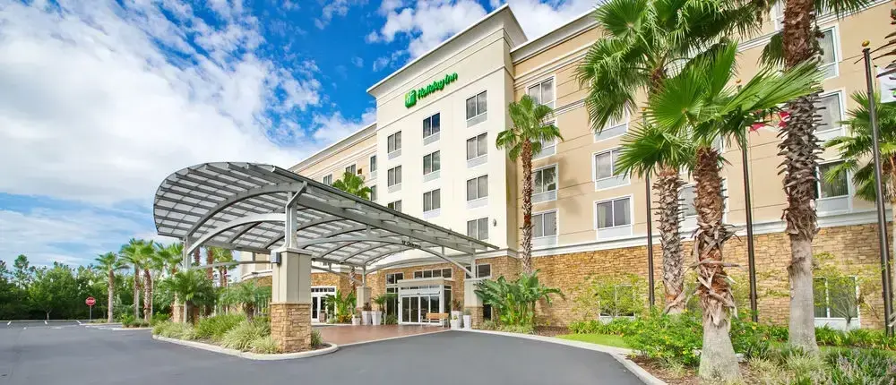 Holiday Inn Titusville hotel exterior with a modern covered entrance, palm trees, and landscaped greenery.