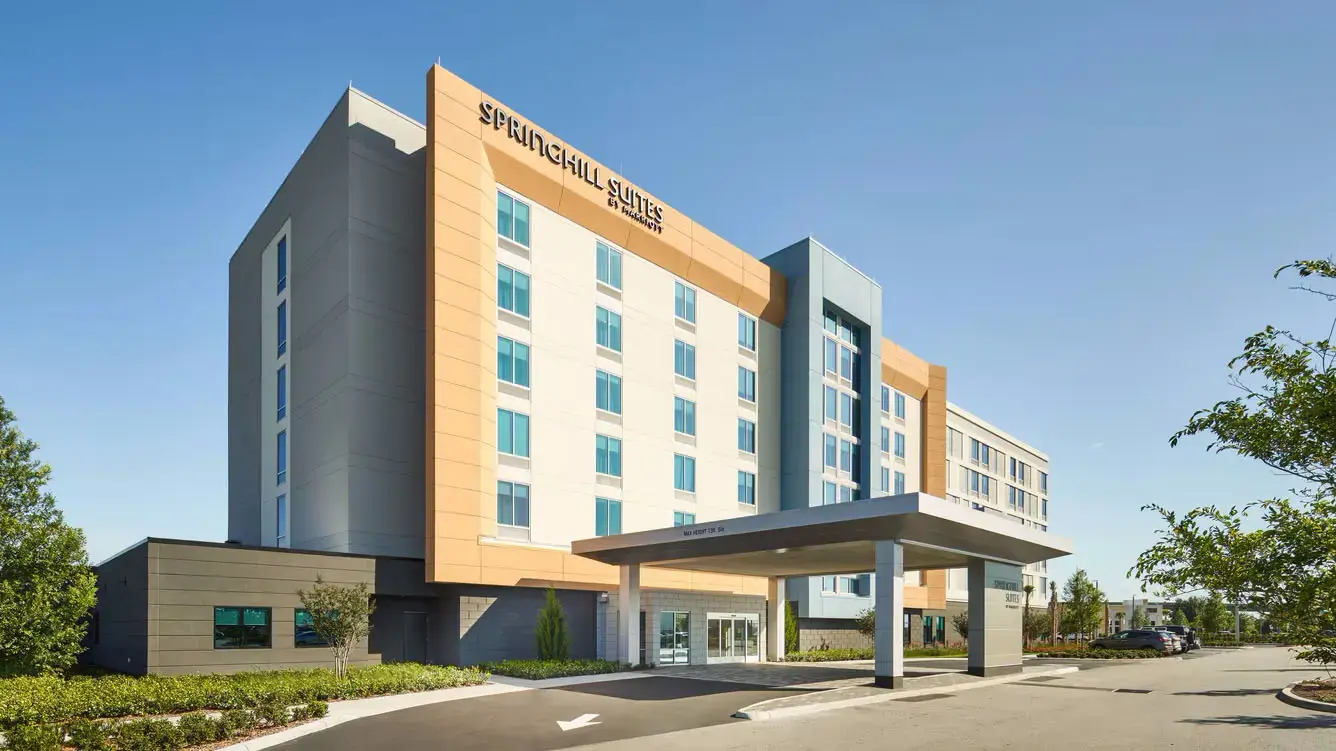 SpringHill Suites by Marriott in Lake Nona, showcasing a modern facade with beige, blue, and orange accents, and a convenient front drive-through entrance.