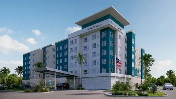 Exterior view of Hyatt House Hotel near Orlando International Airport, featuring a modern multi-story building with teal and white accents, a welcoming entrance, and palm trees under a clear blue sky.