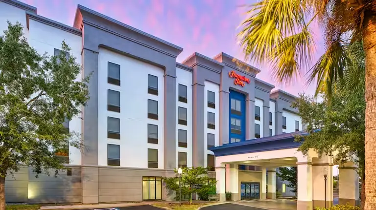 Hampton Inn hotel building featuring a prominent entrance canopy, surrounded by palm trees.