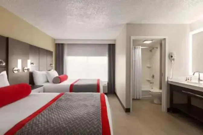 Modern queen room at Ramada Suites featuring  two comfortable queen sized beds with crisp white linens, a stylish headboard, bedside tables with lamps, a work desk, and contemporary decor.