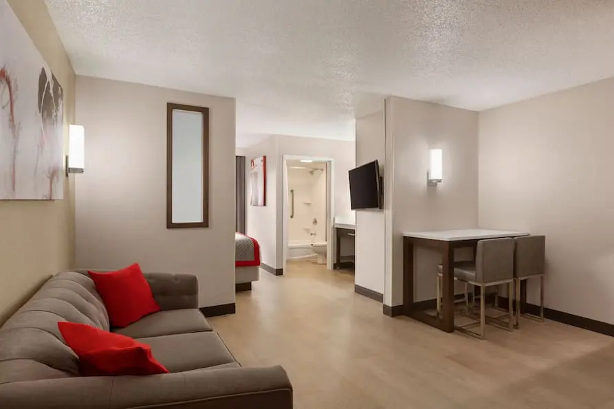 Modern king room at Ramada Suites featuring a comfortable grey couch and dining table.