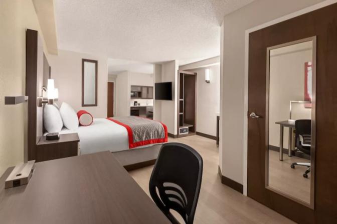 Modern king room at Ramada Suites featuring a comfortable king sized bed a kitchenette and a desk.