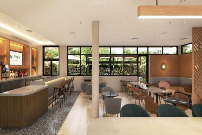 Open dining lounge at EVEN Hotel with natural wood finishes, soft seating, and a mix of table styles, highlighted by large windows offering garden views and ample natural light.