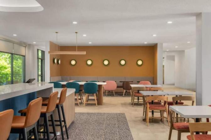 Colorful dining area at EVEN Hotel showcasing a variety of modern chairs, high-top bar seating, and round wall lights against a mustard accent wall, designed for casual social dining.