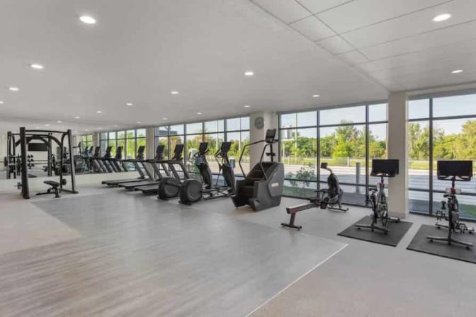 EVEN Hotel's fitness center featuring treadmills, stationary bikes, stair climbers, and resistance training equipment, with floor-to-ceiling windows offering scenic views of surrounding greenery.