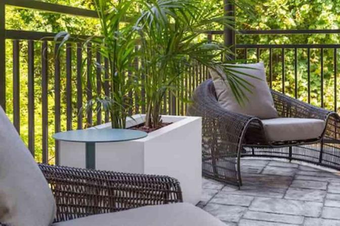 Tranquil outdoor seating area at EVEN Hotel with cushioned wicker chairs, a potted plant on a modern white table, and a private balcony view surrounded by lush green trees.