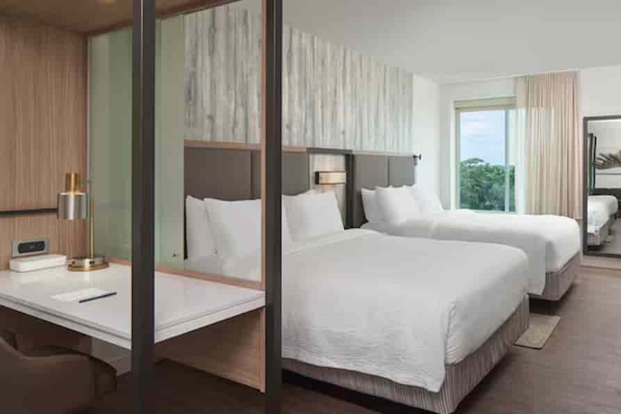 Spacious hotel room with two queen beds, featuring a modern design with a soft color palette and large windows providing natural light.
