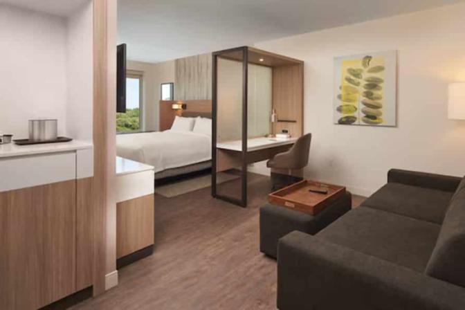 Bright and comfortable hotel room featuring a king bed, sleek decor, and large windows offering natural light and a view of the surrounding area.