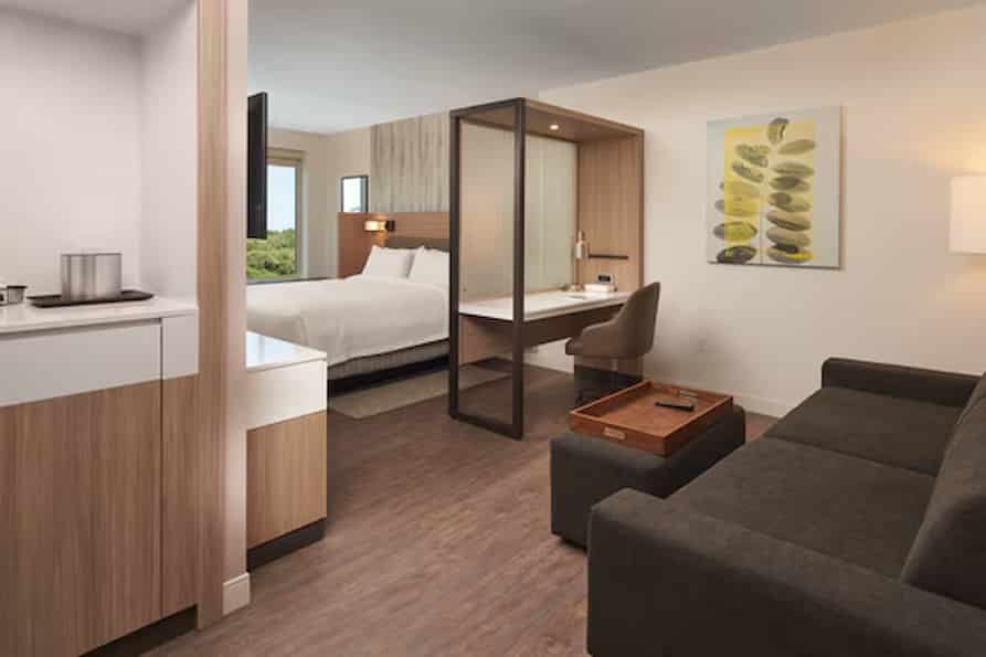 Bright and comfortable hotel room featuring a king bed, sleek decor, and large windows offering natural light and a view of the surrounding area.