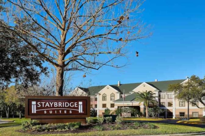 Staybridge Suites Orlando International Airport Hotel building with a large sign in the foreground and a clear blue sky above.