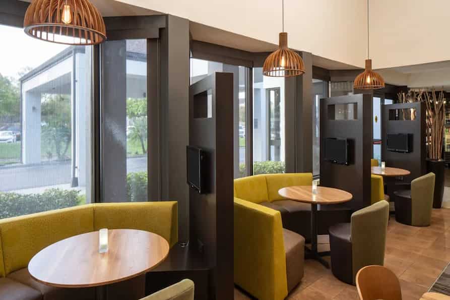 Courtyard by Marriott hotel dining area, featuring three cozy booths with green upholstery, circular tables and modern light fixtures.