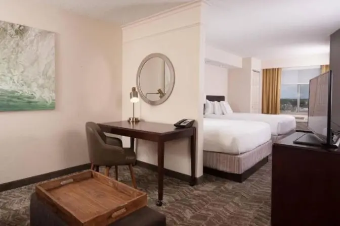 Hotel room at the SpringHill Suites by Marriott featuring two queen beds with white bedding, a desk for work and an ottoman with a wooden tray.