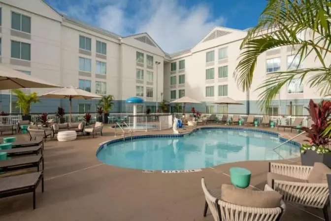 Outdoor pool area at a hotel, including a splash pad for children, lounge chairs, and potted plants.