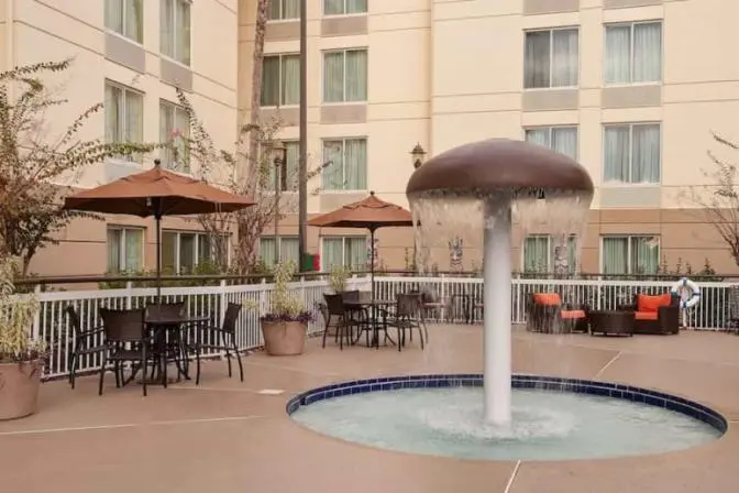 Courtyard with a splash pad water fountain, tables and chairs under umbrellas, and seating areas with orange cushions.
