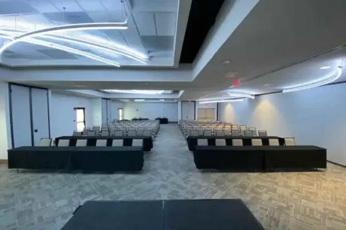 Spacious conference room set up in classroom style with rows of chairs and tables, featuring modern lighting and a neutral color scheme.
