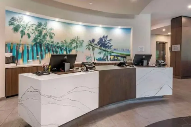 Cambria Orlando International Airport Hotel front desk check in featuring marble countertops and a mural with palm trees.