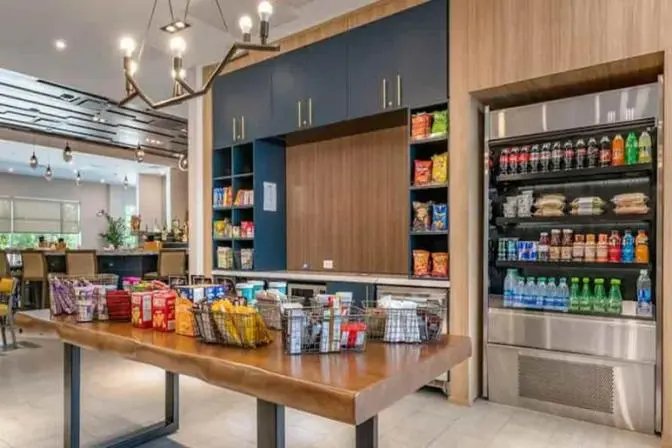 Cambria Orlando International Airport market featuring a large refrigerator full of beverages and grab and go snacks and a large table with packaged snacks.