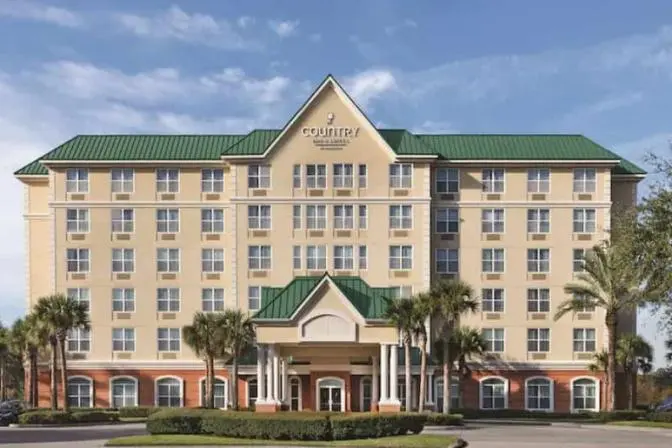 Country Inn & Suites near Orlando Airport, featuring a grand entrance with palm trees and manicured lawn against a warm afternoon sky.