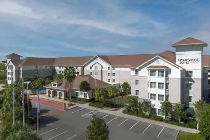 Homewood Suites by Hilton near Orlando Airport, featuring a welcoming exterior with warm afternoon lighting and a spacious parking area.