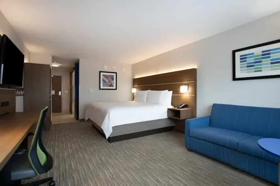 A room that has one King bed and a large blue couch at the Cambria Orlando International Airport hotel.