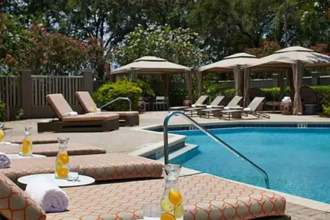 Renaissance Orlando Airport Hotel pool area showcasing cushioned lounge chairs with citrus-infused water pitchers, private cabanas, blooming landscaping, and a tranquil pool with stainless steel handrails.