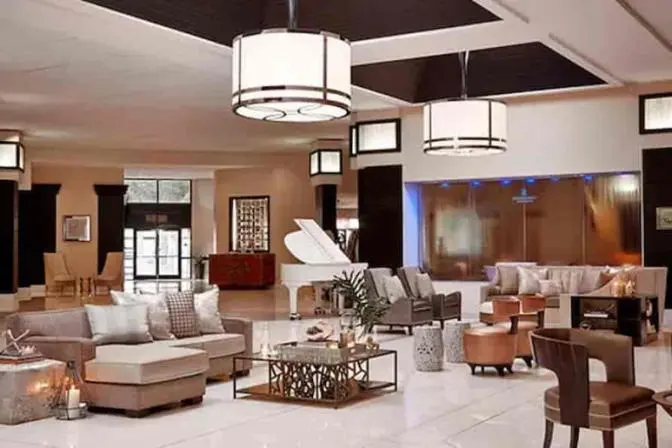 Spacious main lobby at Renaissance Orlando Airport Hotel featuring elegant seating areas, a grand white piano, modern chandeliers, and a tranquil waterfall wall accent behind the lounge.