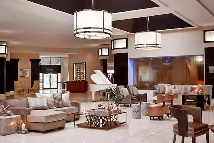 Spacious main lobby at Renaissance Orlando Airport Hotel featuring elegant seating areas, a grand white piano, modern chandeliers, and a tranquil waterfall wall accent behind the lounge.