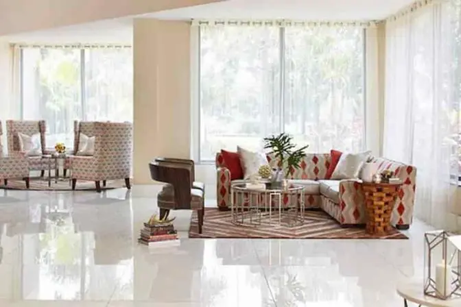 Corner lounge at Renaissance Orlando Airport Hotel with floor-to-ceiling windows, bright natural light, patterned armchairs, and a red-and-white geometric sofa arranged around glass-top coffee tables.