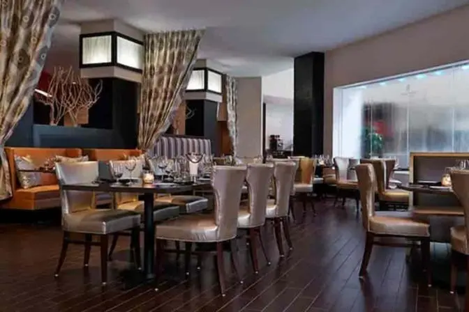 Upscale restaurant at Renaissance Orlando Airport Hotel featuring dark wood flooring, contemporary dining tables, metallic leather chairs, cozy booth seating, and ambient lighting with flowing curtains.