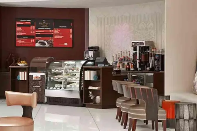 Café at Renaissance Orlando Airport Hotel offering espresso drinks, pastries, and snacks, with a coffee bar counter, menu boards, refrigerated display case, and modern seating in a relaxed lobby setting.