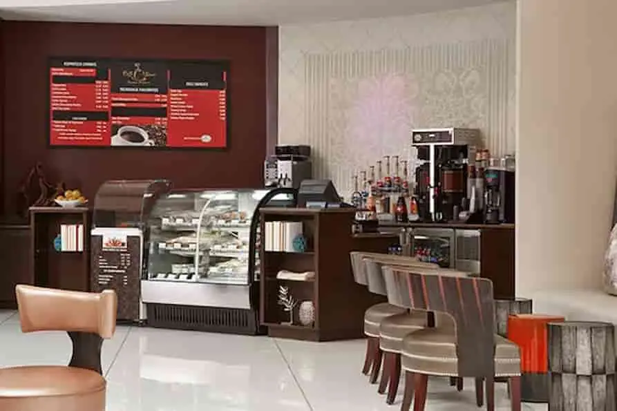 Café at Renaissance Orlando Airport Hotel offering espresso drinks, pastries, and snacks, with a coffee bar counter, menu boards, refrigerated display case, and modern seating in a relaxed lobby setting.