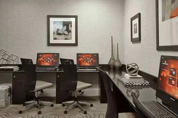 Renaissance Orlando Airport Hotel business center featuring individual computer workstations with rolling mesh chairs, modern art decor, and a wraparound black desk for guests' convenience.