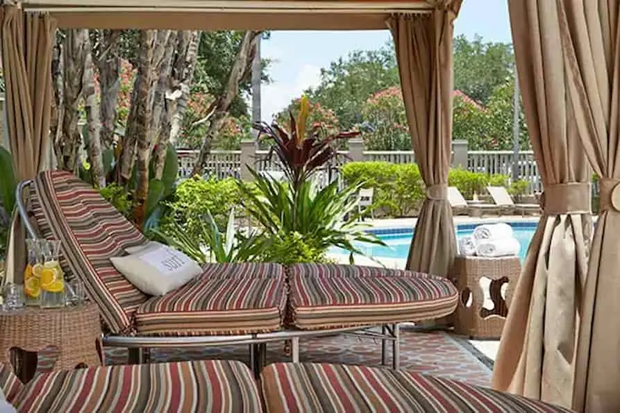 Private cabana area at Renaissance Orlando Airport Hotel with striped cushioned lounge chairs, tropical plants, citrus-infused water pitchers, and pool views surrounded by lush landscaping.