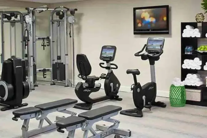 Hotel fitness center at Renaissance Orlando Airport featuring cardio equipment, strength machines, free weights, and a wall-mounted TV, with fresh towels and refreshments available for guests.