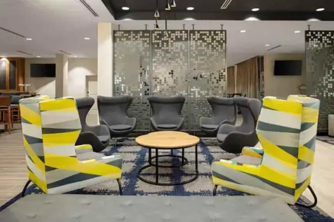 Large lobby area of TownePlace Suites near Orlando Airport, featuring bright colored and funky patterned yellow and navy comfortable chairs circles around a wooden coffee table