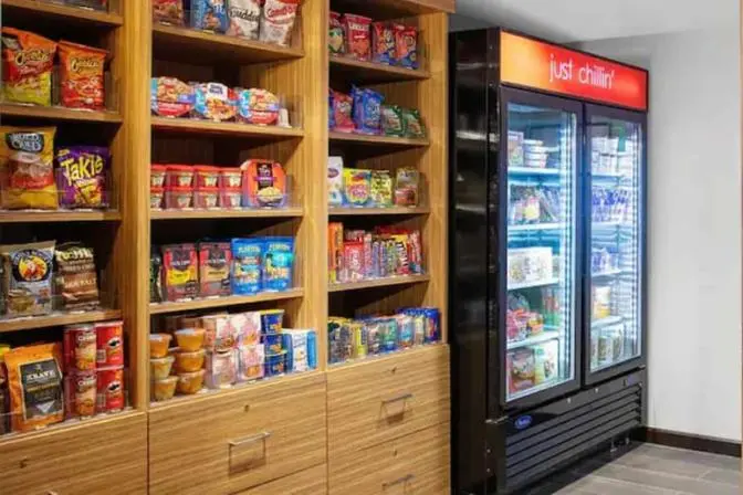 TownePlace Suites near Orlando Airport market featuring a large refrigerator full of beverages and grab and go snacks and a large table with packaged snacks.