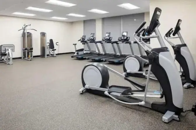 Bright and spacious gym featuring cardio equipment along a large window allowing lots of natural light when the window shades are open.