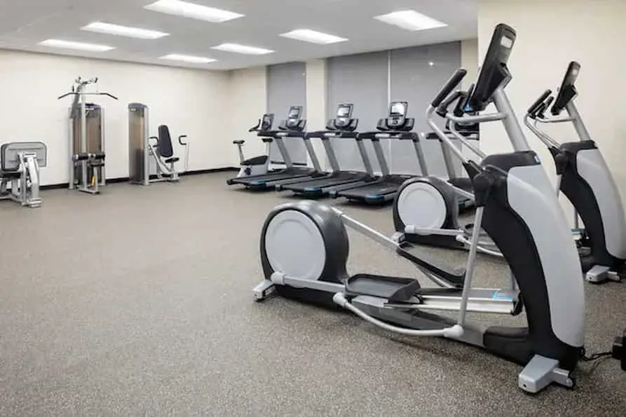 Bright and spacious gym featuring cardio equipment along a large window allowing lots of natural light when the window shades are open.