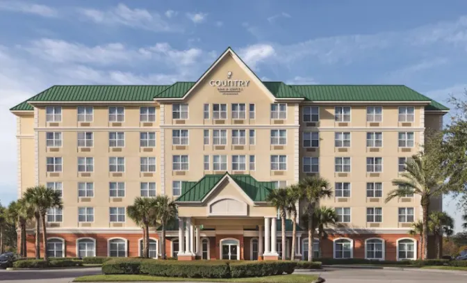 Country Inn & Suites near Orlando Airport, featuring a grand entrance with palm trees and manicured lawn against a warm afternoon sky.