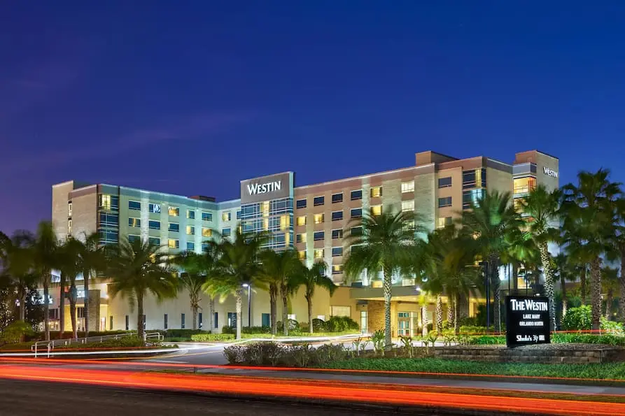 Exterior view of Westin Lake Mary, Orlando North at night, showcasing a modern multi-story building lined with palm trees and illuminated signage