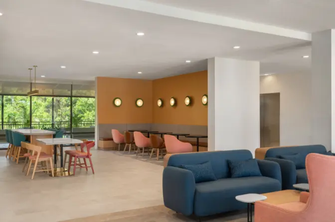 Open dining lounge at EVEN Hotel with natural wood finishes, soft seating, and a mix of table styles, highlighted by large windows offering garden views and ample natural light.