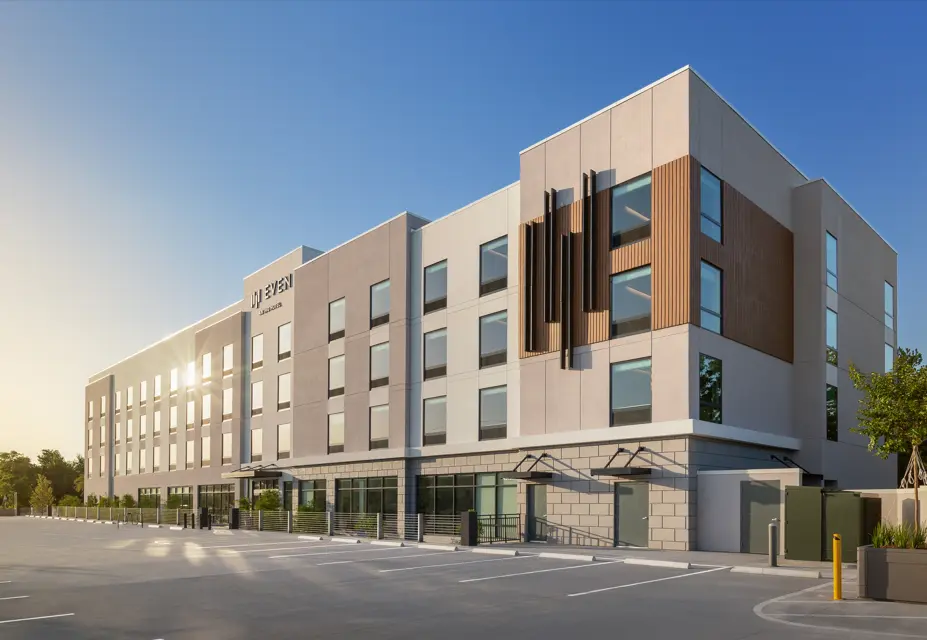 Modern exterior of EVEN Hotel during daylight, showcasing a four-story building with geometric design elements, large grid windows, and an expansive guest parking area.